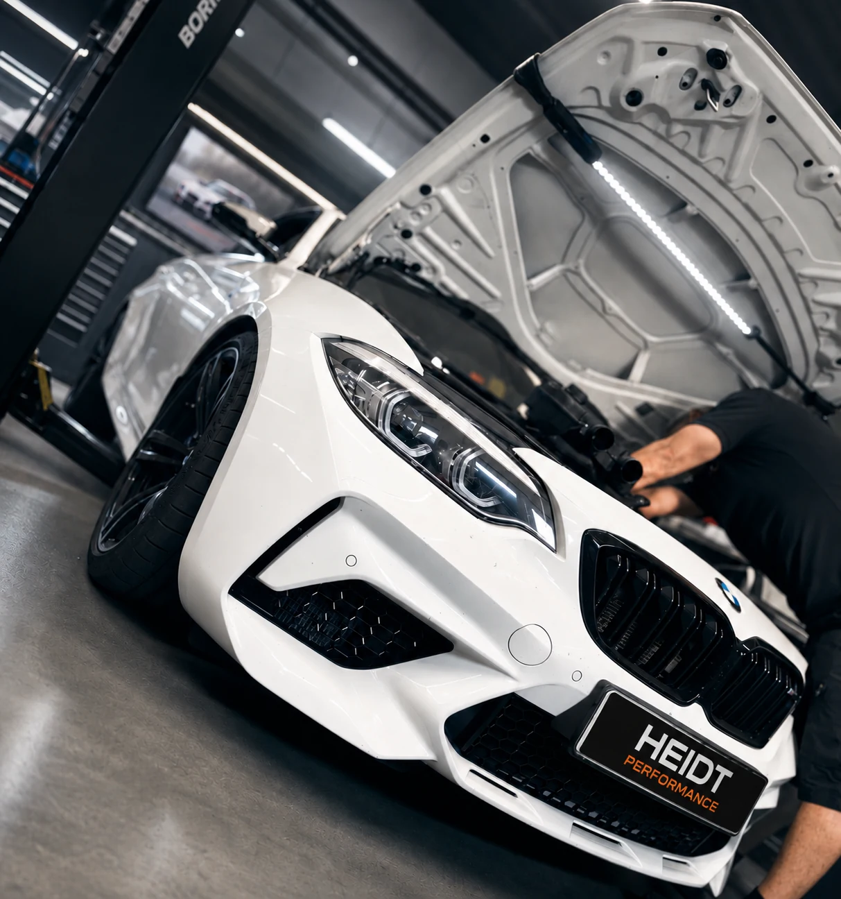 Weißer BMW mit geöffneter Motorhaube und HEIDT Performance Kennzeichen bei der Arbeit in der Werkstatt